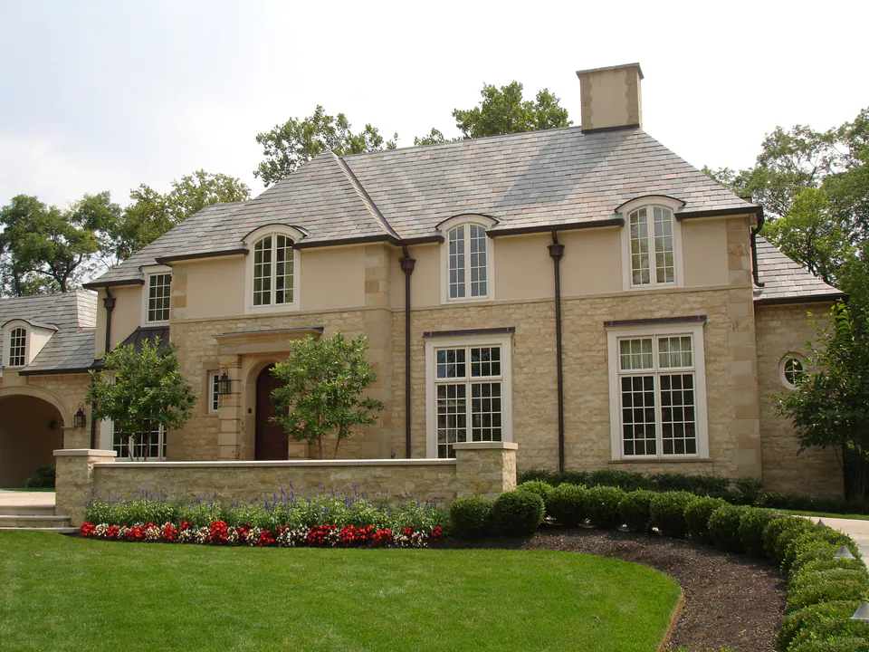 Stone-fronted house with a low stone wall, red and white annuals, clipped shrubs, and a maintained lawn