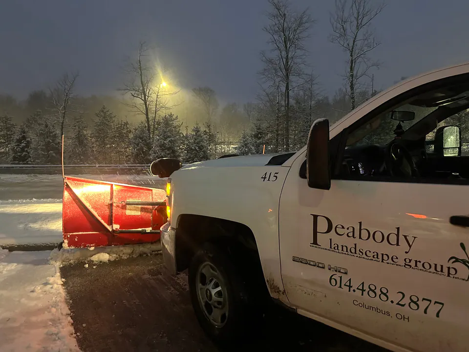 Peabody Landscape Group plow truck with a red blade down at the edge of a snow-covered lot at night