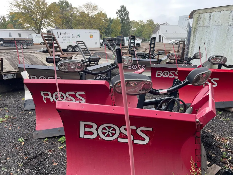 Row of red plow blades staged at the Peabody yard with company trailers behind