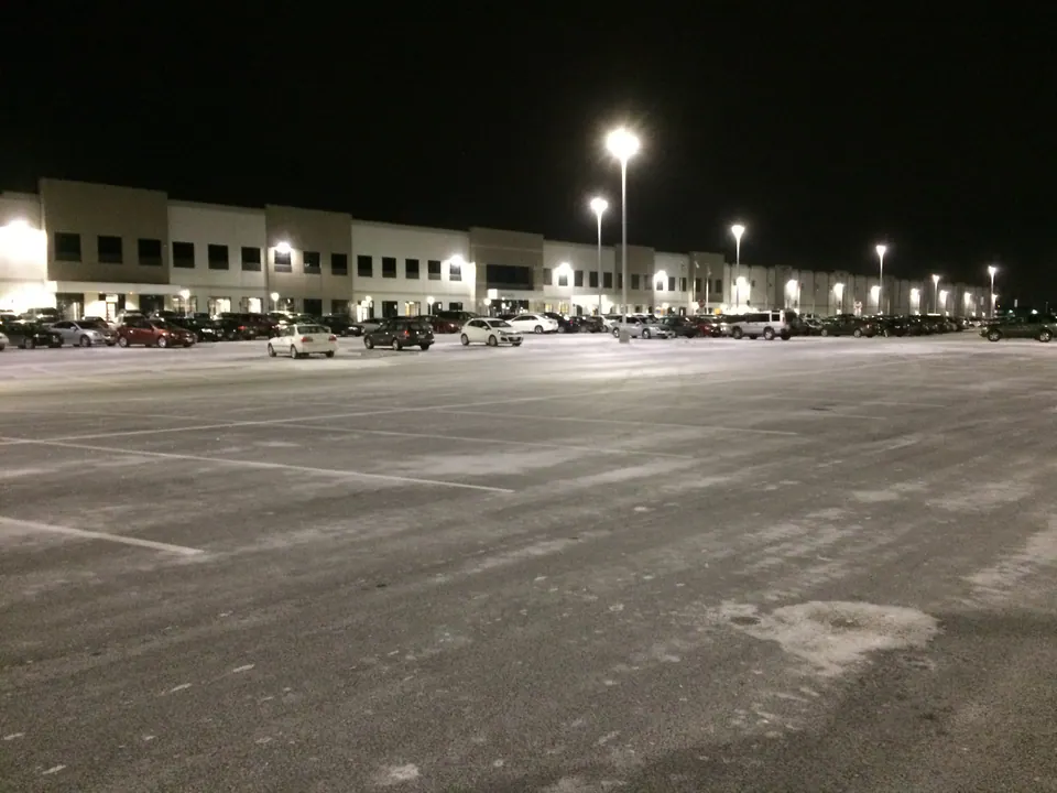 Wide parking lot cleared and treated at night in front of a lit distribution building